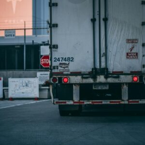 Semi truck parked at a loading dock with visible caution signs and industrial surroundings.